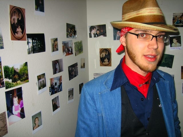 Well dressed young man in Olympia, WA stands in front of wall covered with photographs.